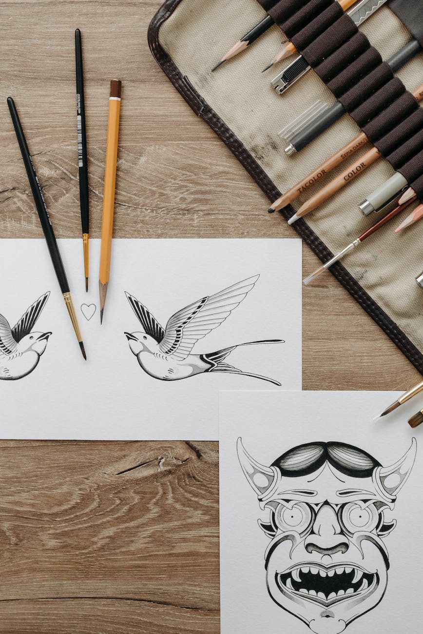 sketches of tattoo design on paper beside drawing materials