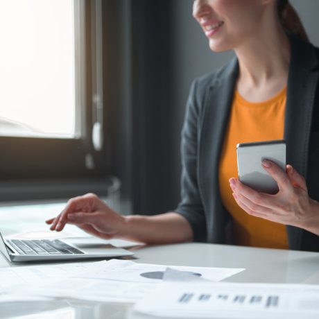 Close,Up,Female,Hand,Keeping,Phone,While,Typing,In,Modern Close up female hand keeping phone while typing in modern laptop in office. Technology and job concept